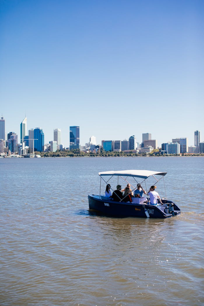 Anonymous group of tourists in roofed boat on ocean enjoying contemporary skyscrapers in town under blue sky